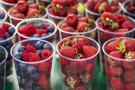 Fresh strawberry and cherry berries in plastic cup in the counterの写真素材