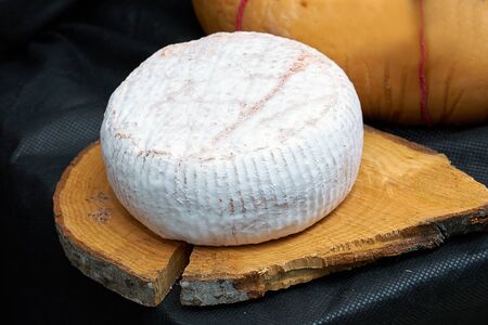 Big head of cheese in a white mold lying on a wooden board, black backgraundの写真素材
