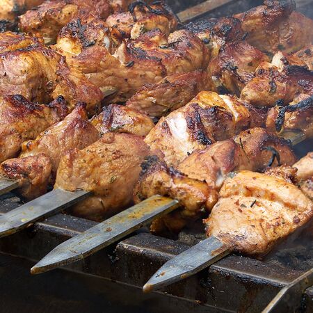 pieces of meat are friend on fire on skewers on grill. close upの写真素材