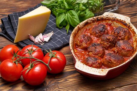 Meatballs in tomato saucel. rustic table. ceramice bowl. black napkin with white cage. piece of hard cheese, fresh basel, garlicの写真素材