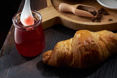 A spoon in a jar of raspberry jam and a croissant on a dark background Board. The jam drips from the spoon. Rustic styleの写真素材