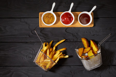 French fries and country potatoes in a basket and three different sauces: Ketchup, Mustard and...