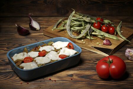 green beans and tomatoes with cheese in a baking dish on a wooden rustic table. Healthy food concept. heart-shaped tomato on the table. dark brown backgroundの写真素材