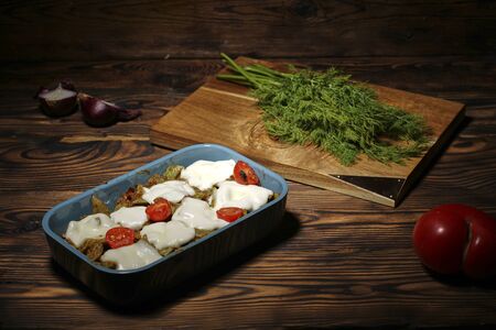 green beans and tomatoes with cheese in a baking dish on a wooden rustic table. Healthy food concept. dill on a wooden Board. dark brown backgroundの写真素材