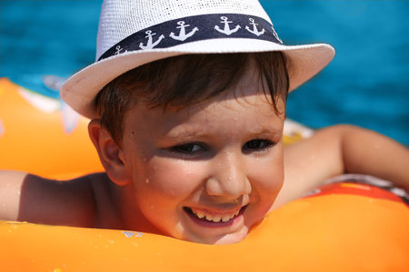 Happy Child on an orange inflatable circle floating on the blue sea, around the spray