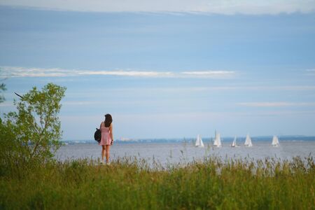 A girl on the beach looks at the sailing yachts in the seaの写真素材