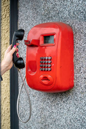 Woman using a public red telephone reaching out with her hand to take the handset off the cradleの写真素材