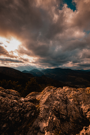 Scenic top view on the valley between the mountains, hills covered with vegetation, forest, storm clouds and sunlightの写真素材