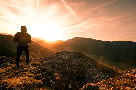 Man stands on the peak of a mountain and watching to Sun. Beautiful moment the miracle of nature during Sunset in Austriaの写真素材