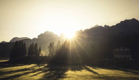 Mountains in morning sunrise light with sun flare in the dolomites italy during summerの写真素材