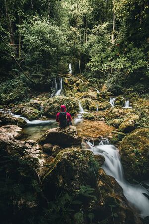 Hiker standing in front of a waterfall surrounded by rocks in the forest in austria in autumnの写真素材