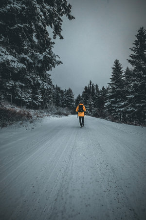 Young man walking in winter landscape on forest path in yellow jacket in austria