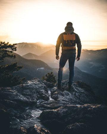 Hiker with backpack standing on top of a mountain and enjoying sunrise in the austrian alps