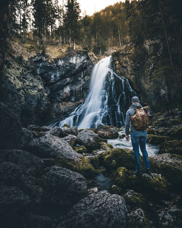 man with backpack standing in front of gollinger waterfall in austriaの写真素材