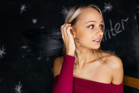 A young blonde girl with bare shoulders looks to the side. Portrait of a cutie on a dark background. High quality photoの写真素材