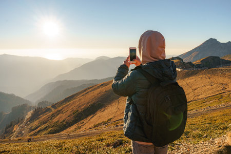 a guy takes pictures with a smartphone of a magnificent landscape on the top of the mountain. High quality photoの写真素材