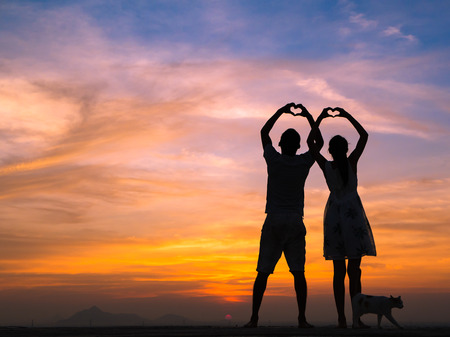 Loving couple showing heart symbol on hands,twilight backgroundの写真素材