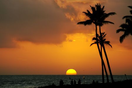 Tropical sunset over the ocean with palm trees and people silhouettes in the foregroundの写真素材
