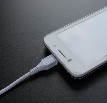 White Smart Phone Charging with USB Cable on the Black Tableの写真素材