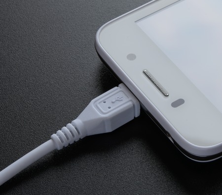 White Smart Phone Charging with USB Cable on the Black Tableの写真素材
