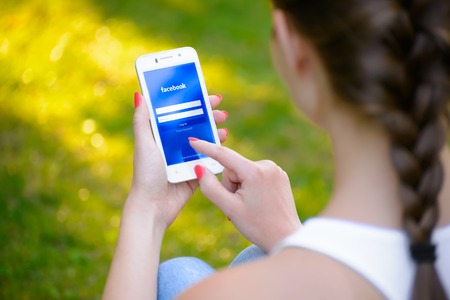 ZAPORIZHZHYA, UKRAINE - SEPTEMBER 20, 2014: Young Woman Using Facebook Social Network Application on her Smart Phone.のeditorial素材