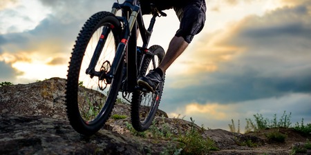 Cyclist Riding the Bike Down Rocky Hill at Sunset. Close up Extreme Sport Concept. Space for Text.