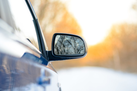 Close up Image of Side Rear-view Mirror on a Blue Car in the Winter Landscape with Evening Sunの写真素材