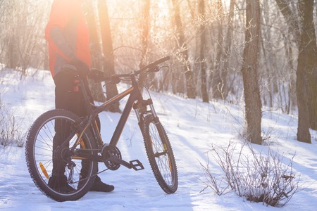 Mountain Biker with his Bike on the Snowy Trail in the Beautiful Winter Forest Lit by the Sunの写真素材