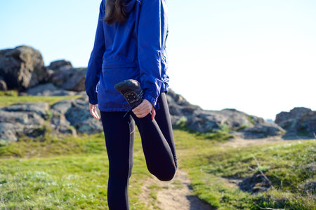 Young Fitness Woman Stretching her Legs on the Rocky Trail in Sun Rays. Female Runner Doing...
