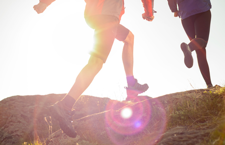 Young Couple Running on the Rocky Trail in the Mountains at Sunset or in the Morning. Active Lifestyle Conceptの写真素材