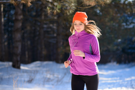 Young Woman Running in the Beautiful Winter Forest at Sunny Frosty Day. Active Lifestyle Concept.の写真素材