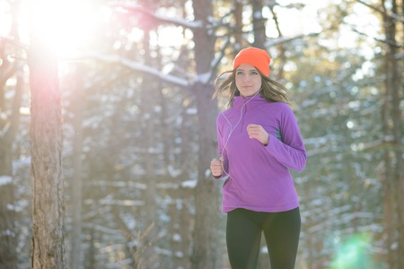 Young Woman Running in Beautiful Winter Forest at Sunny Frosty Day. Active Lifestyle Concept.の写真素材
