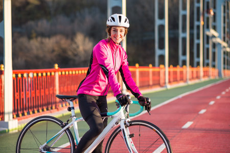 Portrait of Young Smiling Female Cyclist in Pink Jacket Resting with Road Bicycle in the Cold Sunny...