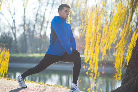Young Male Runner Stretching in the Park in Cold Sunny Autumn Morning. Healthy Lifestyle and Sport...