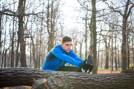 Young Male Runner Stretching in the Park in Cold Sunny Autumn Morning. Healthy Lifestyle and Sport Concept.の写真素材