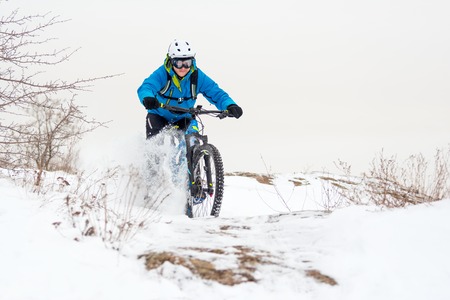 Cyclist in Blue Riding the Mountain Bike on the Rocky Winter Hill Covered with Snow. Extreme Sport and Enduro Biking Concept.の写真素材