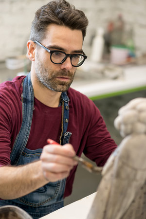 Portrait of Ceramist Dressed in an Apron Working on Clay Sculpture in Bright Ceramic Workshop.の写真素材