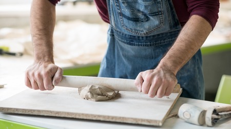 Ceramist Dressed in an Apron Working with Raw Clay in Bright Ceramic Workshop.の写真素材
