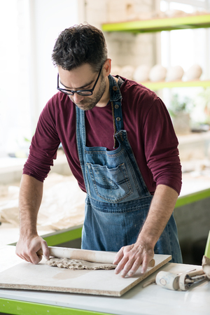 Ceramist Dressed in an Apron Working with Raw Clay in Bright Ceramic Workshop.の写真素材