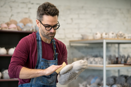 Portrait of Ceramist Dressed in an Apron Working on Clay Sculpture in Bright Ceramic Workshop.の写真素材