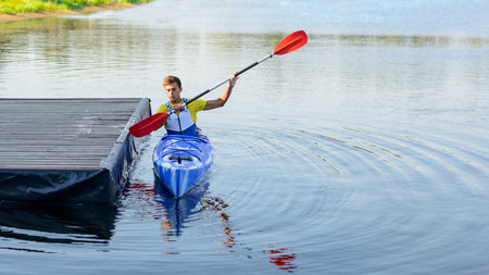 Young Professional Kayaker Paddling Kayak on the River under Bright Morning Sun. Sport and Active Lifestyle Conceptの写真素材