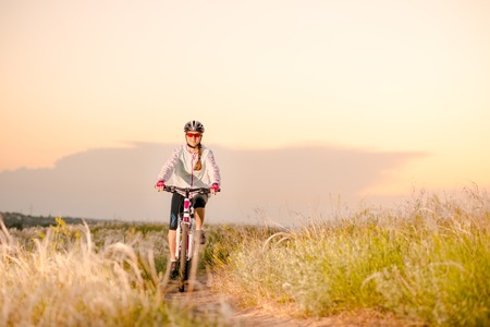 Young Woman Riding the Mountain Bikes in the Beautiful Field Full of Feather Grass at Sunset. Adventure and Travel Concept.の写真素材