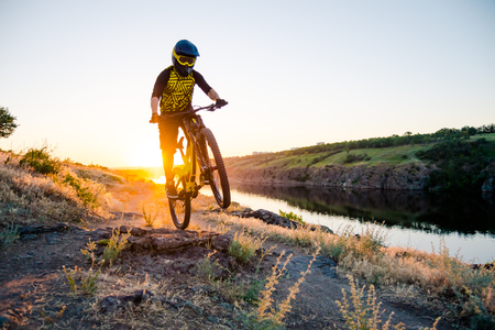 Professional Cyclist Riding the Downhill Mountain Bike on the Summer Rocky Trail at Sunset. Extreme Sport and Enduro Cycling Concept.の写真素材