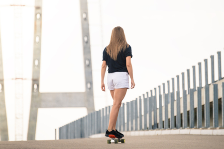 Young Beautiful Blonde Girl Riding Orange Skateboard on the Bridgeの写真素材