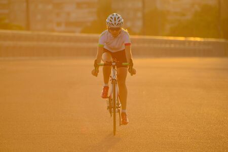 Young Woman Riding Road Bicycle on Free Street in the City at Sunset. Healthy Lifestyle and Sport Concept.の写真素材