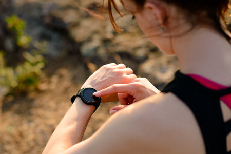 Young Woman Runner Using Multisport Smartwatch at Sunset Trail. Closeup of Hand with Fitness...