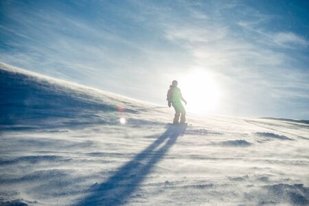 Silhouette of Snowboarder Riding Snowboard in the Mountains at Sunny Day in the Snowstorm. Snowboarding and Winter Sportsの写真素材