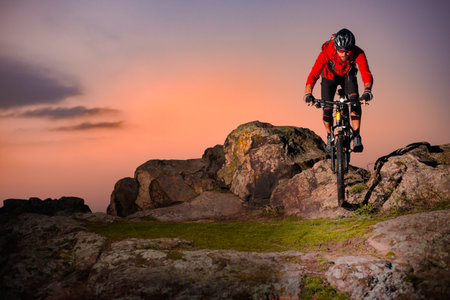 Cyclist in Red Riding Bike on the Spring Rocky Trail at Sunset. Extreme Sport and Enduro Biking Concept.の写真素材