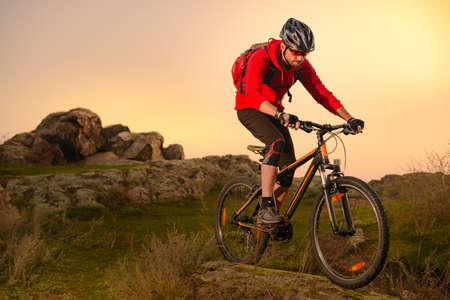 Cyclist in Red Riding Bike on the Spring Rocky Trail at Sunset. Extreme Sport and Enduro Biking Concept.の写真素材