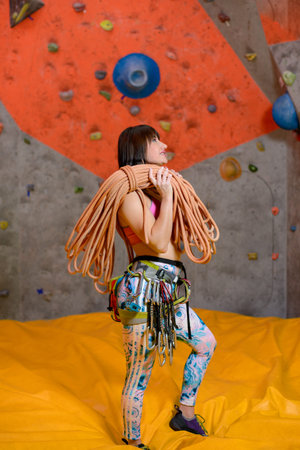 Young Smiling Woman Climber with Rope and Carbines in Climbing Gym. Extreme Sport and Indoor Climbing Conceptの写真素材